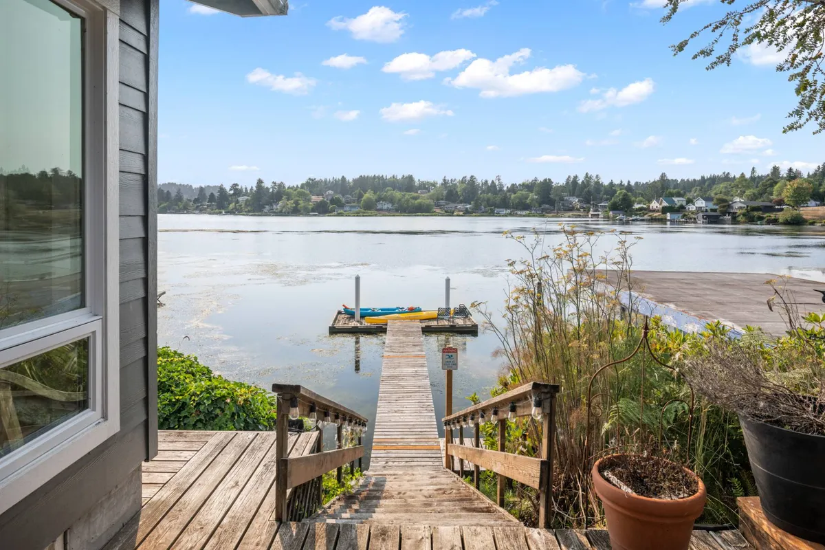 A tranquil scene of a wooden dock reaching over calm lake waters, surrounded by greenery. The dock is the focal point, suggesting opportunities for kayaking, fishing, or simply relaxing by the water’s edge as the sun rises or sets.