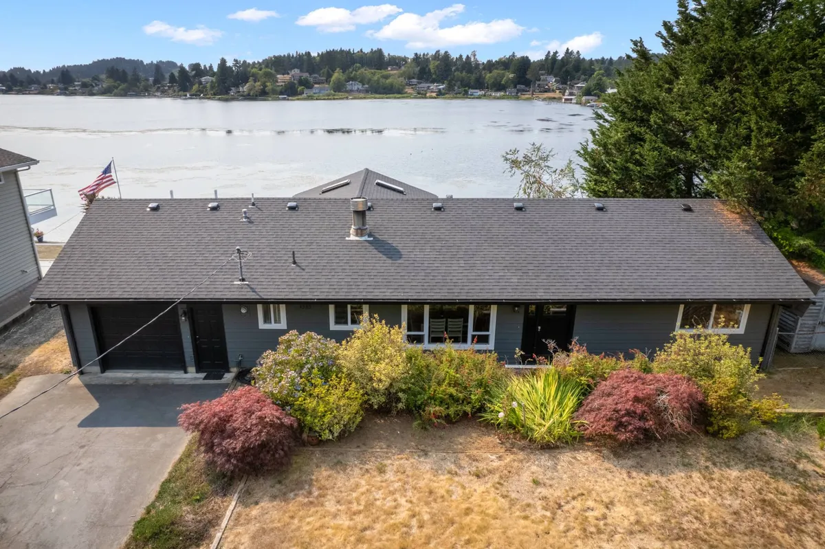 The house’s facade opens to a lush garden and an expansive view of the water beyond. The scene is peaceful, with the possibility of relaxing by the water visible and the garden area suggesting an easy indoor-outdoor lifestyle.