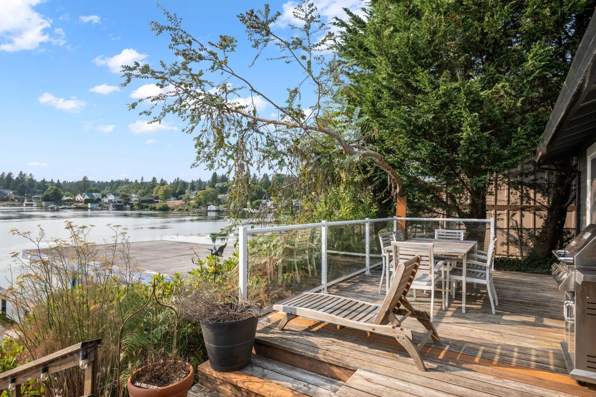 This image features a comfortable deck area with outdoor furniture overlooking a tranquil water view, framed by lush greenery. The serene setting invites guests to relax, dine outdoors, or simply take in the natural beauty right from their lakeside base.