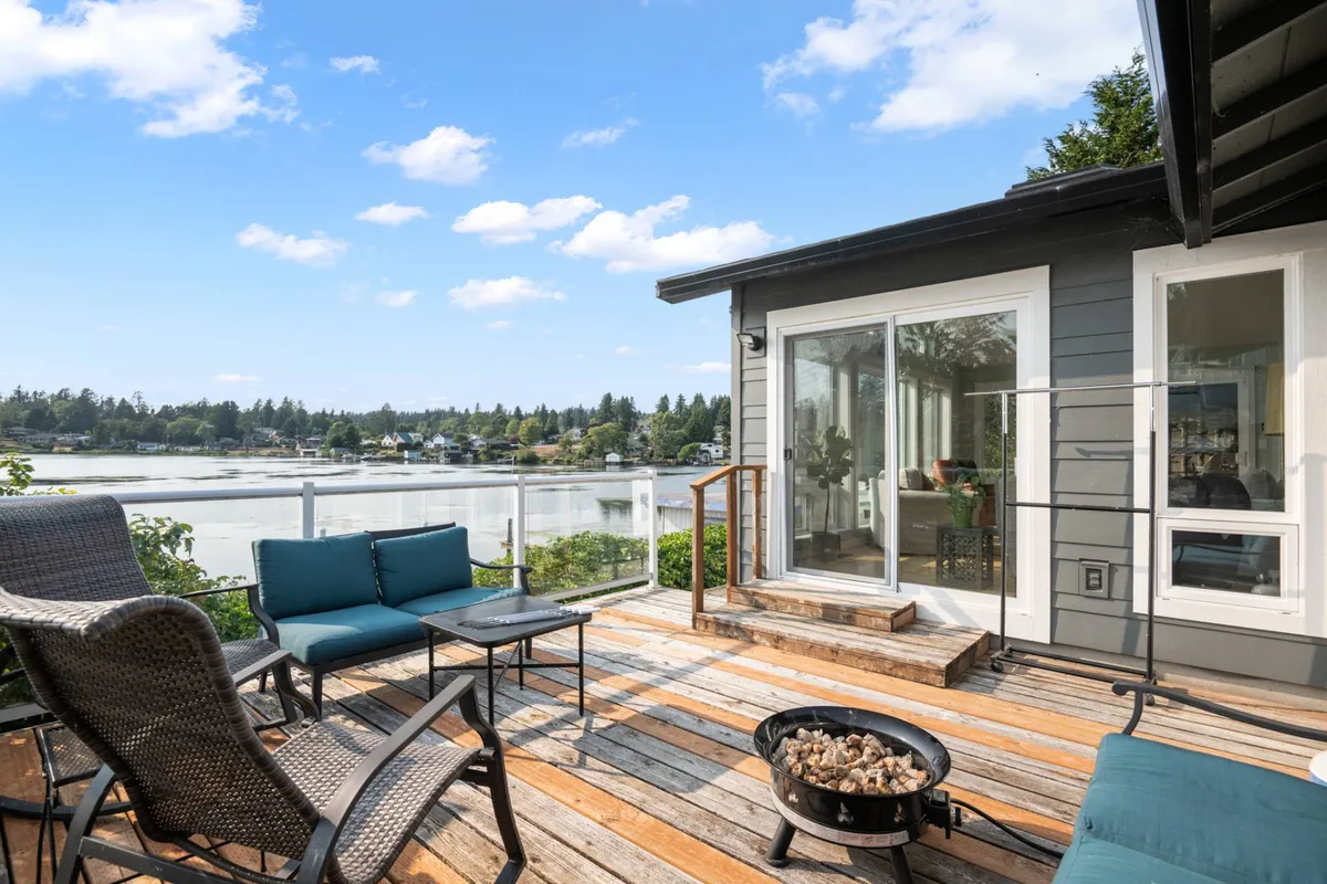 A tranquil outdoor seating area with Adirondack chairs gathered around a fire pit, all overlooking a stunning water view. The space is surrounded by grass and open sky, perfect for relaxing, entertaining, or unwinding with pets after a day of lakeside fun.