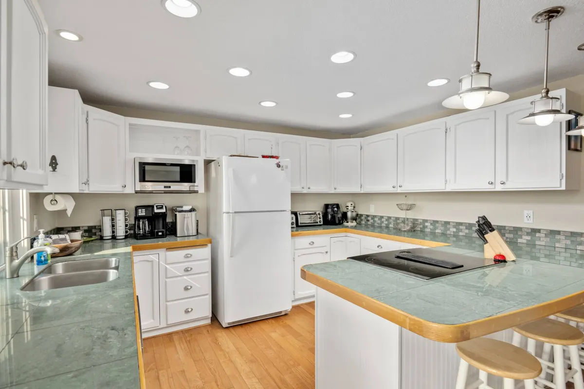 A modern kitchen with crisp white cabinets, a green countertop, stainless steel appliances, and a central island. The space is lively yet comfortable, ideal for cooking, entertaining, and family gatherings. The arrangement spotlights areas for baking, meal prep, and group interaction, illustrating a fully-stocked kitchen set up for holiday treats or casual breakfasts.