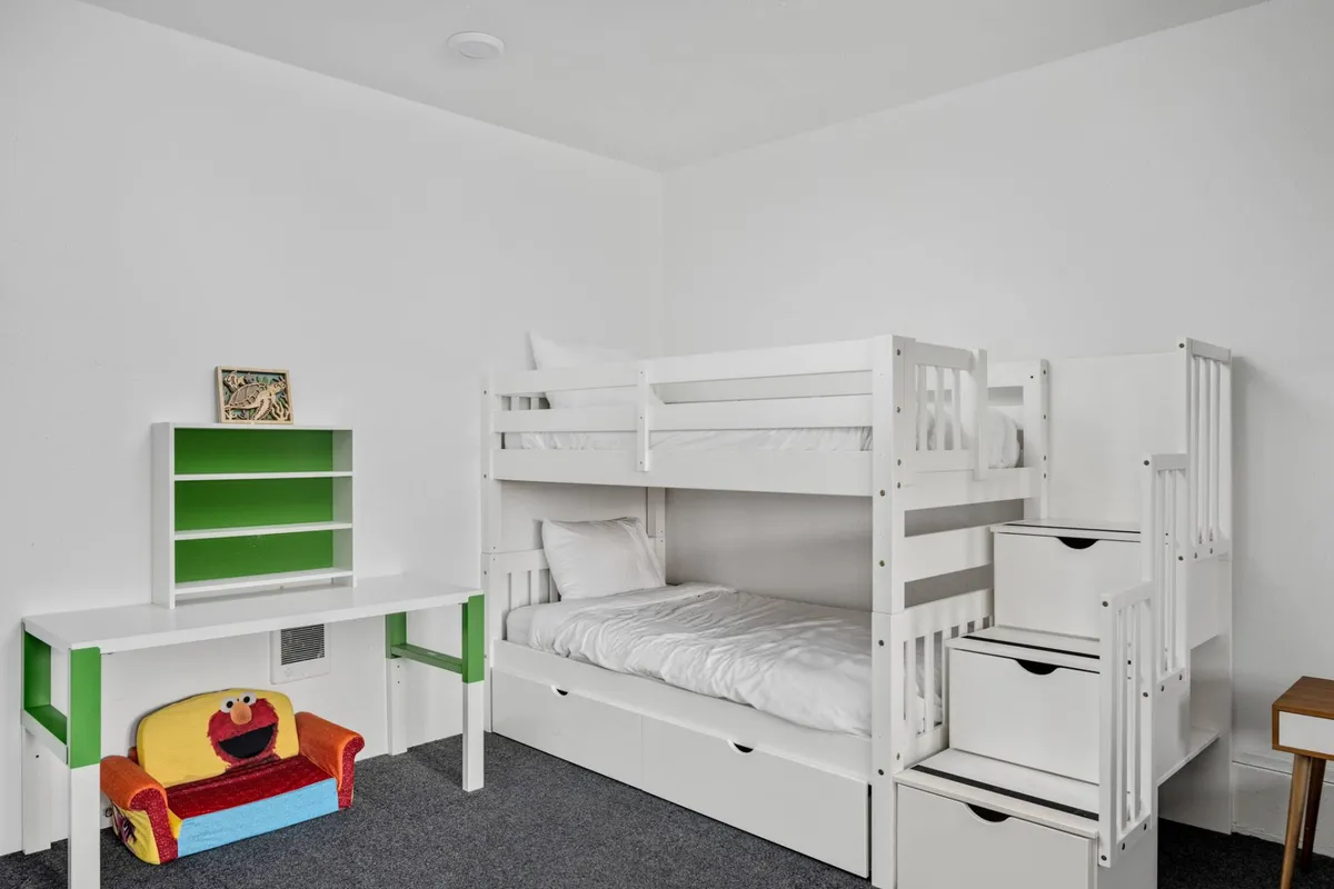 A cheerful, flexible room with a bunk bed, colorful chair, and a desk with shelving. The playful atmosphere and practical layout make it ideal for both sleep and play, catering to kids or teens. The room is functional, with vibrant touches that create a sense of fun and flexibility.