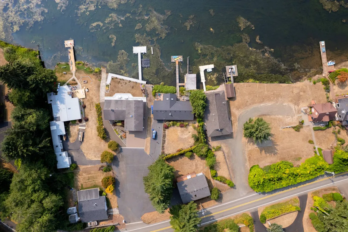 A view down the shoreline featuring several waterfront properties, docks, and a gently curving roadway surrounded by greenery. The setting is serene, with visible walking paths and open areas that invite exploration, strolls, and playtime near the water's edge.