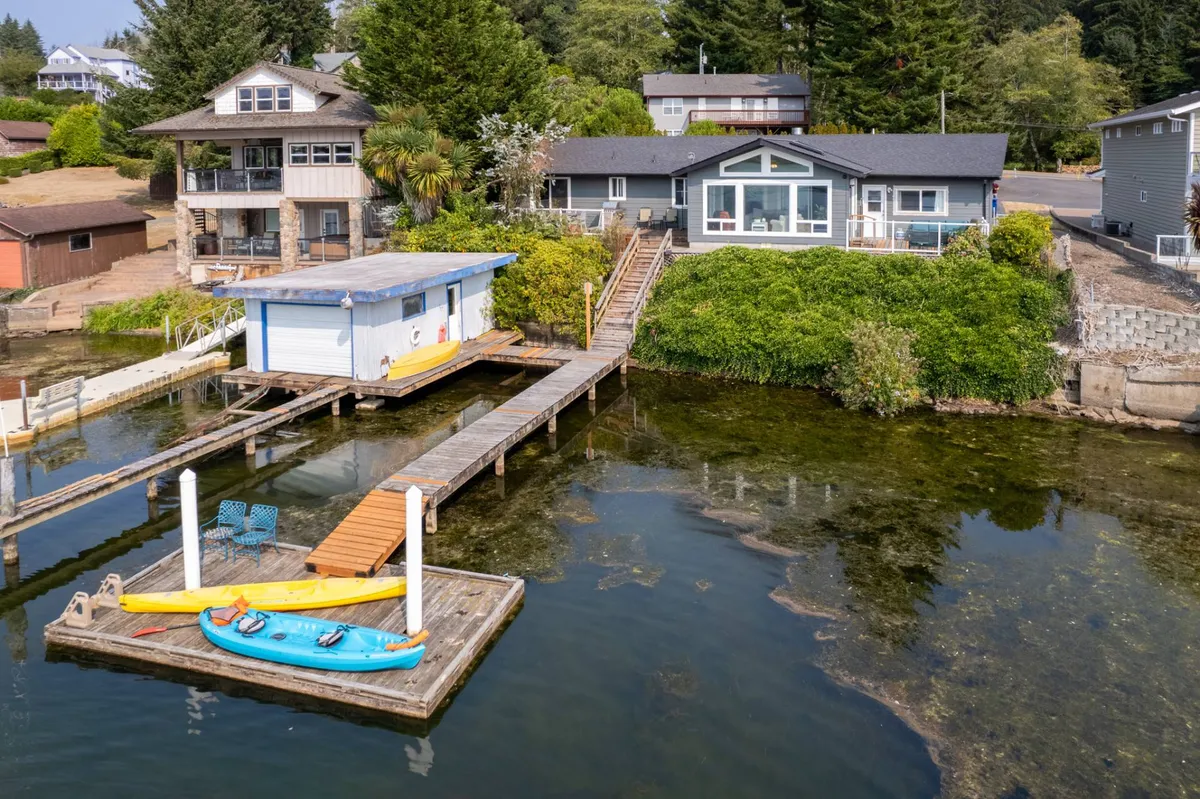 This image features the main house, a prominent dock extending into the water, colorful kayaks ready for use, and a charming boathouse, all set against lush greenery. The peaceful atmosphere invites guests to imagine launching watercraft or relaxing by the lakeside.